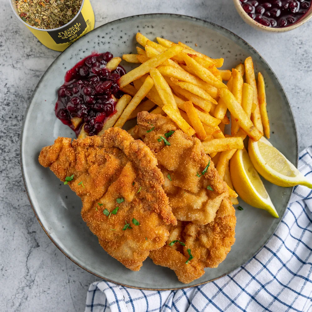 Zwei panierte Schnitzel mit Pommes, Preiselbeeren und Zitrone